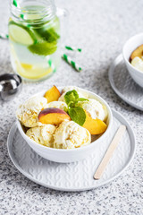  Homemade peach ice cream with mint and fresh peach slices in a plate on a gray background