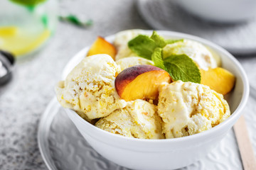  Homemade peach ice cream with mint and fresh peach slices in a plate on a gray background