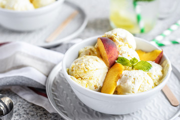  Homemade peach ice cream with mint and fresh peach slices in a plate on a gray background
