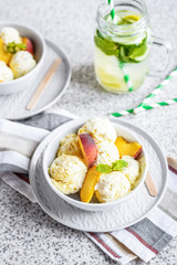  Homemade peach ice cream with mint and fresh peach slices in a plate on a gray background