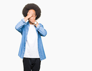 Young african american man with afro hair Covering eyes and mouth with hands, surprised and shocked. Hiding emotion