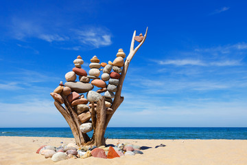 stack of multicolored balanced stones on an old wooden snags, on a blue sky and sea background