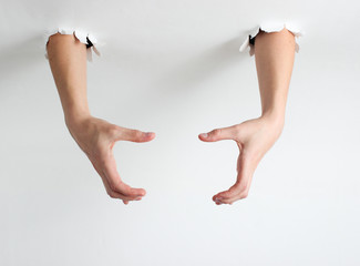 Female hands through the torn holes of a white background. Copy space. Creative art