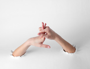 Woman stretches her fingers through the torn holes of a white background. Creative art