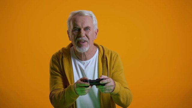 Emotional senior man with joystick playing videogame, upset with round result