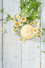 chamomile flowers and baby cream on white wooden table, directly above