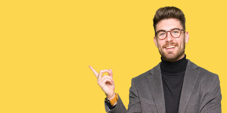 Young handsome business man wearing glasses with a big smile on face, pointing with hand and finger to the side looking at the camera.