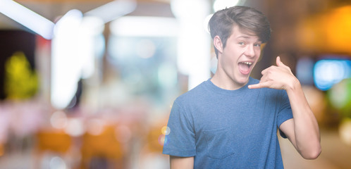 Young handsome man wearing blue t-shirt over isolated background smiling doing phone gesture with hand and fingers like talking on the telephone. Communicating concepts.
