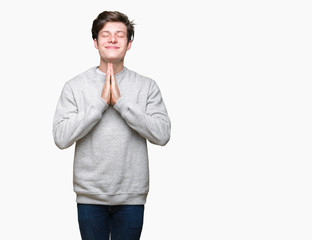 Young handsome sporty man wearing sweatshirt over isolated background praying with hands together asking for forgiveness smiling confident.