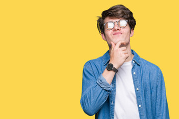 Young handsome man wearing glasses over isolated background looking confident at the camera with smile with crossed arms and hand raised on chin. Thinking positive.