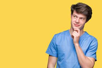 Young doctor wearing medical uniform over isolated background with hand on chin thinking about question, pensive expression. Smiling with thoughtful face. Doubt concept.