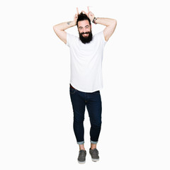 Fototapeta premium Young hipster man with long hair and beard wearing casual white t-shirt Posing funny and crazy with fingers on head as bunny ears, smiling cheerful