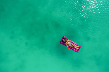 Aerial view of slim woman swimming on the swim mattress in the transparent turquoise sea. Summer...