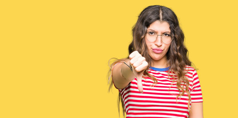 Young beautiful woman wearing glasses looking unhappy and angry showing rejection and negative with thumbs down gesture. Bad expression.