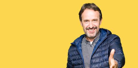 Fototapeta premium Middle age handsome man wearing winter coat smiling friendly offering handshake as greeting and welcoming. Successful business.