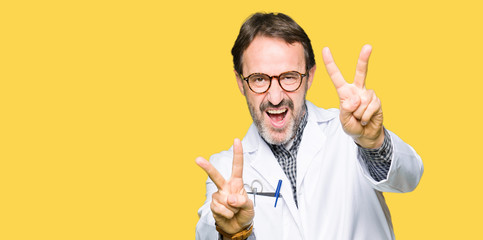 Middle age doctor men wearing medical coat smiling looking to the camera showing fingers doing victory sign. Number two.