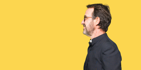 Middle age priest man wearing catholic robe looking to side, relax profile pose with natural face...