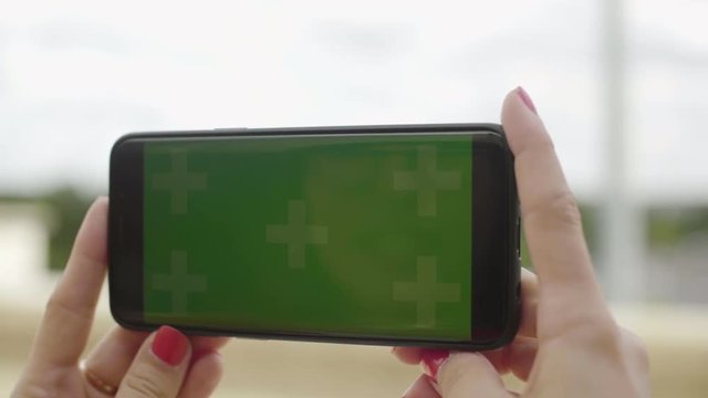 Close-up of smartphone with Green Screen at Eiffel Tower, holding by woman in Horizontal Landscape Mode, watching movie on touch screen with Tracking Markers. Watching Content, Videos, Blogs.