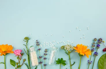 Deurstickers Flat lay view homeopathic medicine pills in jars and spilled around on light blue background, decorated with fresh various herbs and plants, flowers. Homeopathy border background, lot of copy space. © FotoHelin
