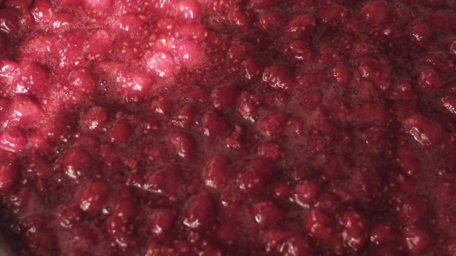 Housewife stirring raspberry jam in an enameled bowl with a wooden spatula.