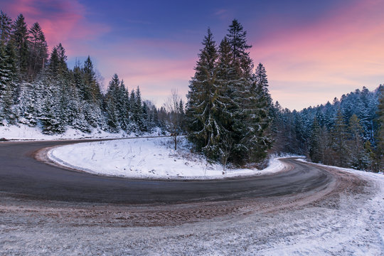 empty serpentine road in mountains. spruce trees along the way. beautiful transportation scenery in winter at dusk. freezing cold weather. red clouds on the deep blue sky. dangerous turnaround