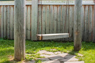old wooden swing on chains between two logs near the wooden fence