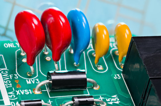 Colorful varistors. Circuit board detail. Electronic components for surge protector. Diodes, red, blue and yellow voltage-dependent resistors on green PCB from dismantled uninterruptible power supply.