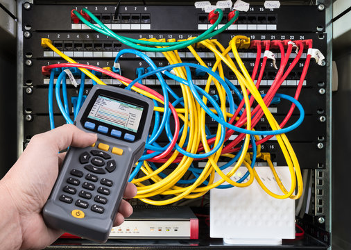 Network test. Qualified cable performance tester in human hand detail. Data signal measurement. Colorful cables connected in patch panels of rack case. Working IT specialist. Professional maintenance.