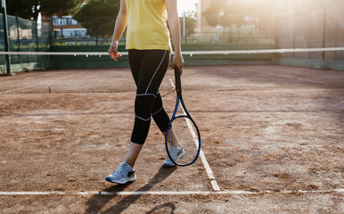 Female tennis player holding the tennis racket on the sunset at the tennis court 