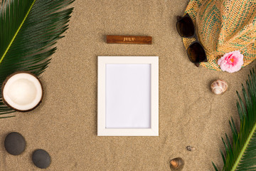 Fototapeta na wymiar Stylish summer composition with photo frame, green leaves, hat and sunglasses on a sand background. Artwork mockup with copy space