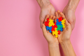 Adult and kid hands holding colorful heart on light pink background. World autism awareness day concept