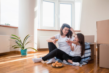 Happy kid near box excited about moving day, cheerful girl sitting with mother on blanket in new home having fun