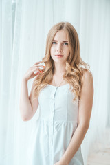 Fototapeta premium Girl in a light white dress posing by the window.