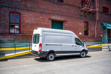 White compact popular cargo mini van for local deliveries and business standing on the warehouse parking lot - obrazy, fototapety, plakaty