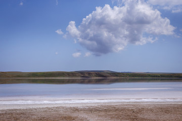 Bright salt deposits on the shore of a beautiful pink lake. Unusual phenomena of nature. In the background mountains and clouds.