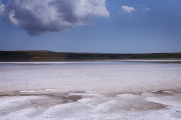 Bright salt deposits on the shore of a beautiful pink lake. Unusual phenomena of nature. In the background mountains and clouds.