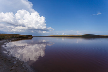 The surface of the pink lake and its shore in the background. Incredible clouds are reflected in the water.