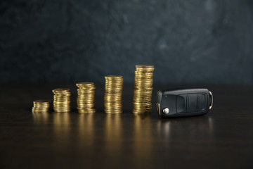 Close-up Of Car Key In Front Of Coins Stacked On Wooden Table