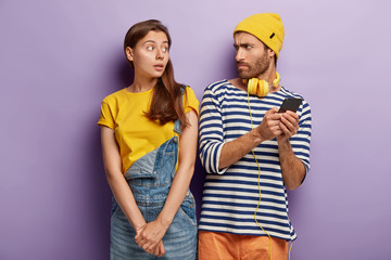 Curious woman wants to have look at friends gadget, angry disappointed man holds mobile phone, doesnt give it to companion, has sullen expression. People, emotions and modern technologies concept