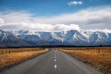 A long straight road path journey towards snow mountains in New Zealand. - obrazy, fototapety, plakaty