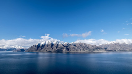 Fototapeta na wymiar New Zealand travel image of Lake Hawea with snow mountain and blue mirror lake. Peaceful image of natural scenery during winter season in South island, New Zealand.