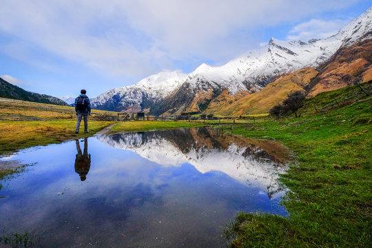 Traveler exploring natural landscape image of snow mountain, blue lake, green grass field in New Zealand. Hiking image at peaceful remote location. Motivational and inspiration use.