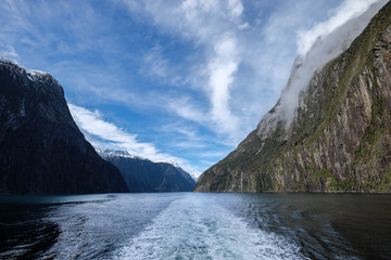 In Milford Sound cruise, one experience the spray of a waterfall close to sheer rock faces. A popular tourist destination and natural landscape in New Zealand. This view is breathtaking and iconic.