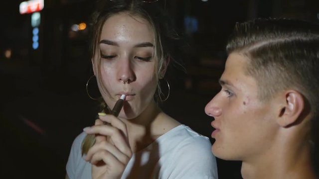 Portrait of a young girl smoking a vape in the face of a guy. Iqos