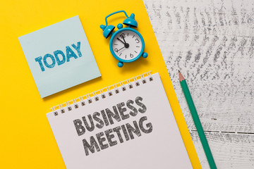 Text sign showing Business Meeting. Business photo showcasing used discuss issues that cannot be addressed in simple way Spiral notepad paper sheet marker alarm clock retro wooden background