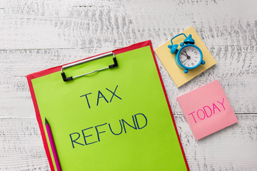 Handwriting text Tax Refund. Conceptual photo refund on tax when the tax liability is less than the tax paid Metal clipboard sheets marker alarm clock notes pad wooden background