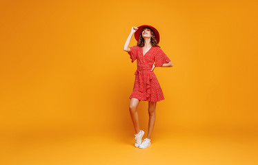 concept happy emotional young woman in red summer dress and hat jumping   on yellow background.