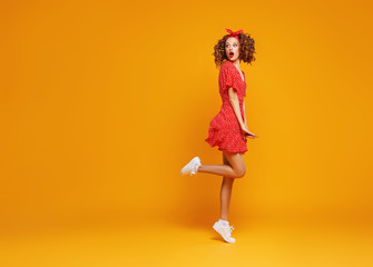 Fototapeta na wymiar concept happy emotional young woman in red summer dress jumping on yellow background