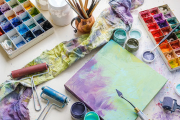 Artistic equipment in studio: canvas, palette knife, paint brushes, paints and palette. Top view.