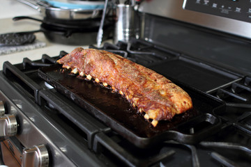 Rack of dry rub pork ribs baked on a cast iron tray, resting on the stove top.